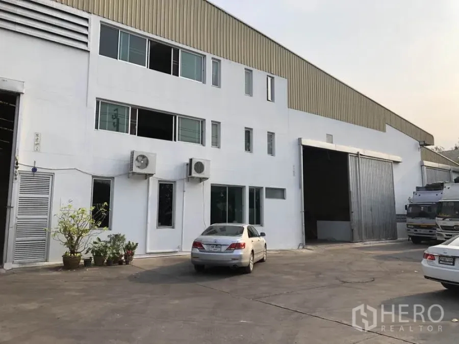 Factory for rent in Bang Bua Thong, Nonthaburi - Two-storey factory exterior in Bang Bua Thong with large sliding warehouse door and on-site parking.