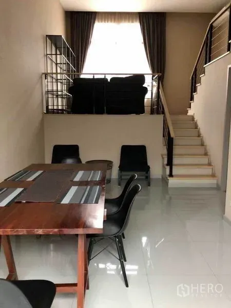 Townhouse for rent in Suan Luang, Bangkok - Split-level dining room with staircase leading to a mezzanine sitting area, glossy tiled floor and tall curtains.
