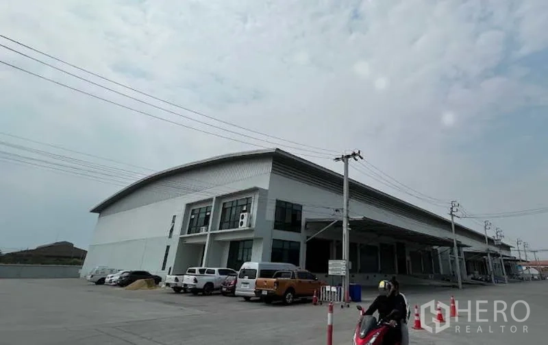 Warehouse for rent in Bang Bo, Samut Prakan - Modern high-clearance warehouse exterior with multiple covered loading bays, raised docking platform, and wide parking area in an industrial zone of Bang Bo, Samut Prakan.
