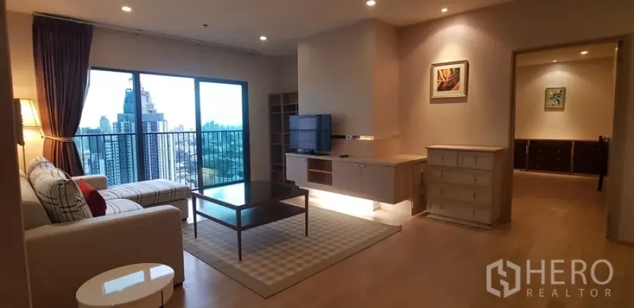 Condominium for rent in Khlong Toei, Bangkok - Spacious living room with sofa, TV console and balcony overlooking the Bangkok skyline.