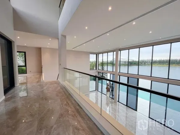 Detached House for sale in Bang Phli, Samut Prakan - Double-height living hall with full-height windows and balcony railing overlooking a peaceful lakeside view.