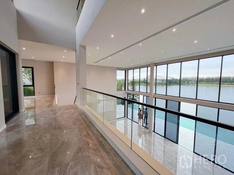 Detached House for sale in Bang Phli, Samut Prakan - Double-height living hall with full-height windows and balcony railing overlooking a peaceful lakeside view.