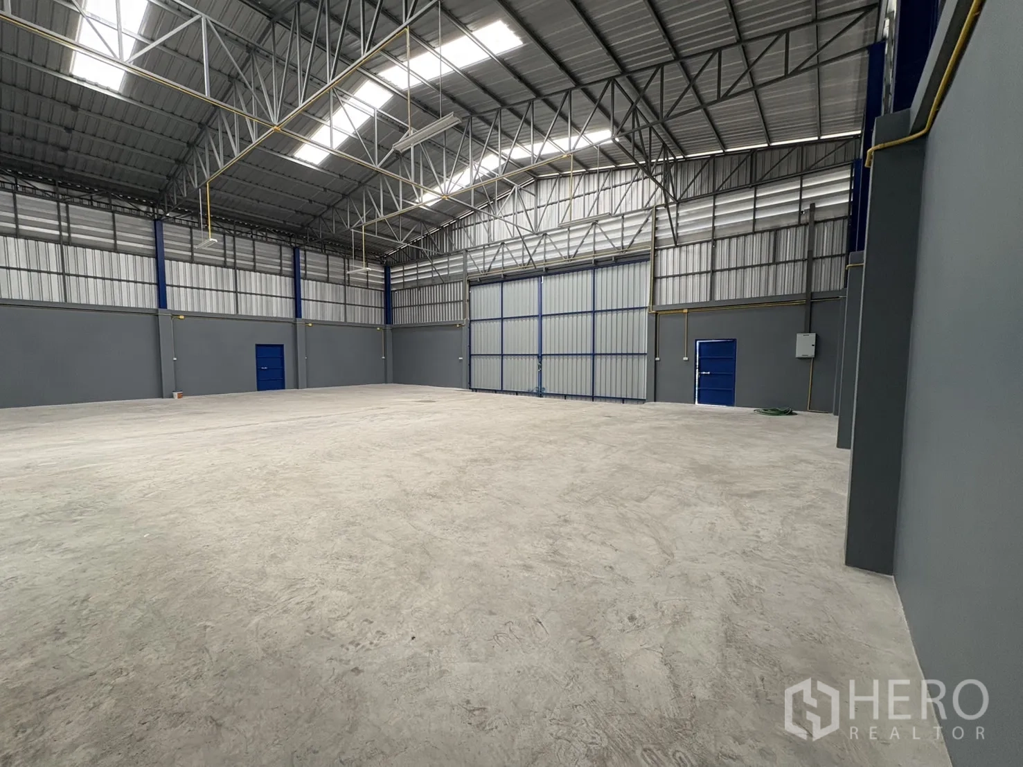 Warehouse for rent in Bang Phli, Samut Prakan - High-clear warehouse with skylights, steel beams, blue access doors, and large sliding entry doors.