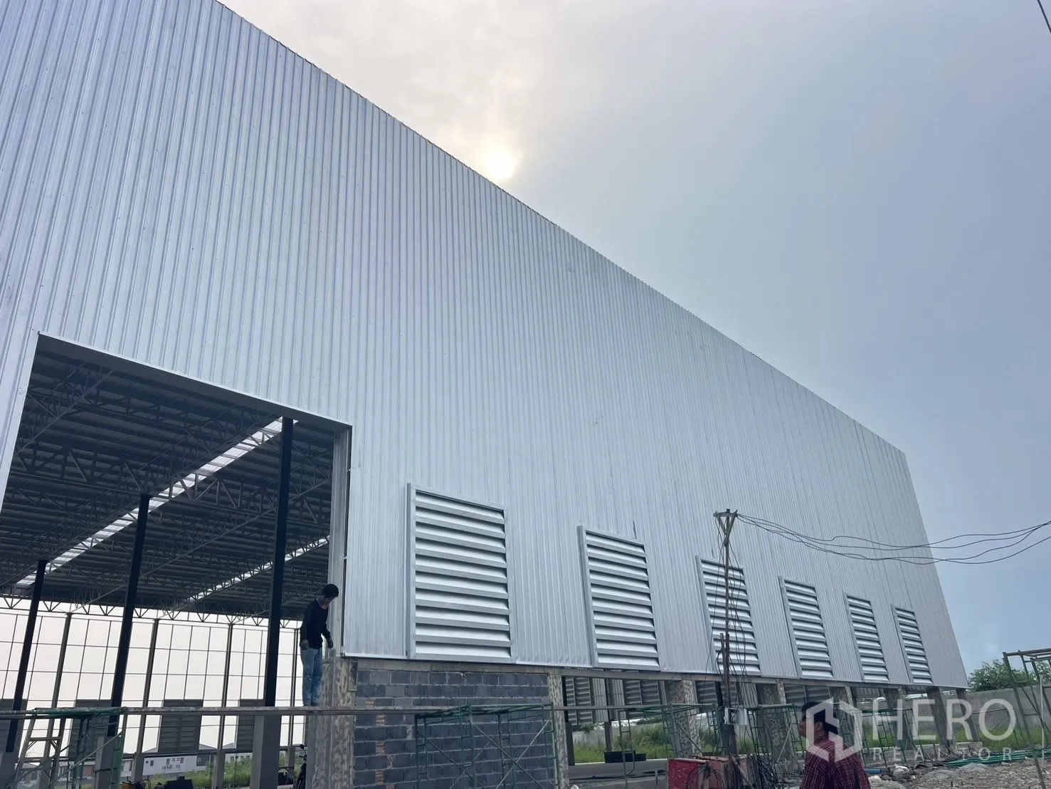 Factory for rent in Mueang Samut Prakan, Samut Prakan - Side elevation of a metal-clad factory with open bay and vents during construction.