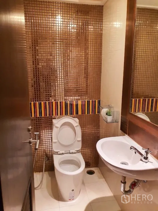 Condominium for rent or sale in Pathum Wan, Bangkok - Compact guest bathroom with mosaic tile wall, large mirror, white basin and toilet.