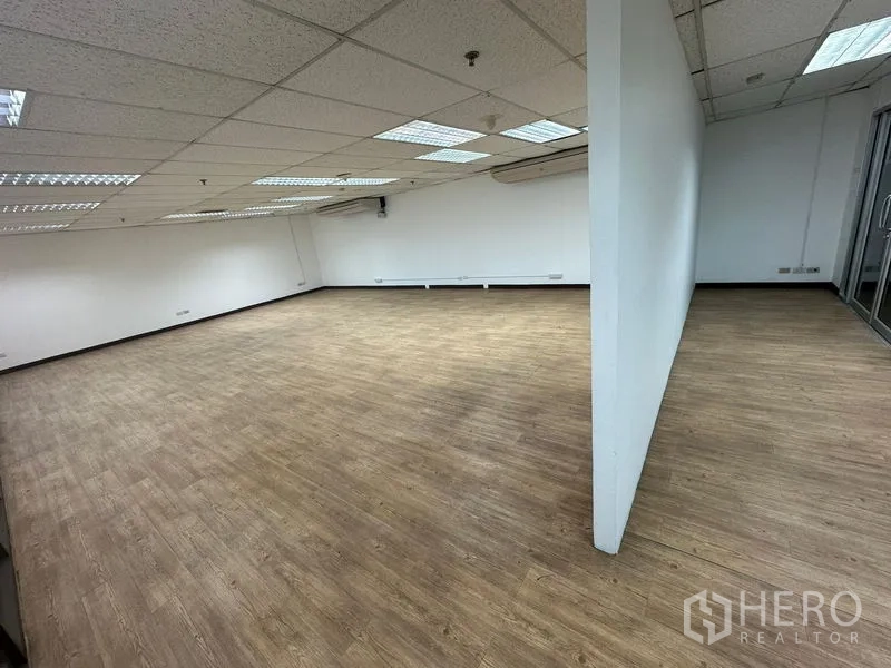 Office Space for rent - Open office area divided by a partial wall, vinyl wood floors, and suspended ceiling lighting.