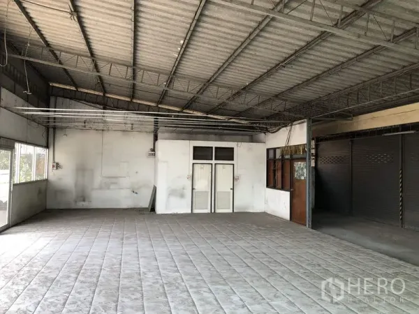 Warehouse for rent in Khlong Luang, Pathum Thani - Open-plan interior with tiled floor, steel truss roof and small office doors.