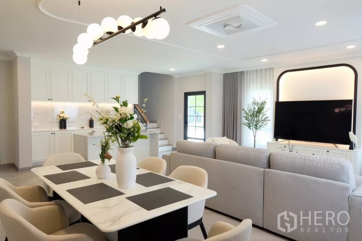 Detached House for sale in Bang Phli, Samut Prakan - Dining table facing the kitchen and staircase, with large sofa under a ceiling cassette air-conditioner