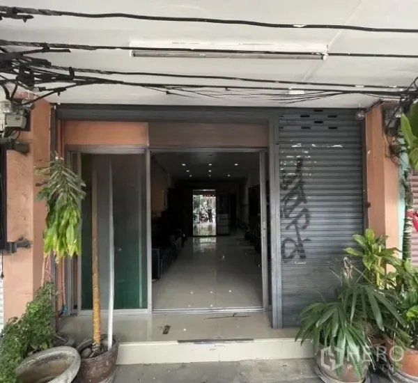 店屋 出租在Phra Khanong, Bangkok - 临街商铺门面，推拉玻璃门、金属卷闸与盆栽。