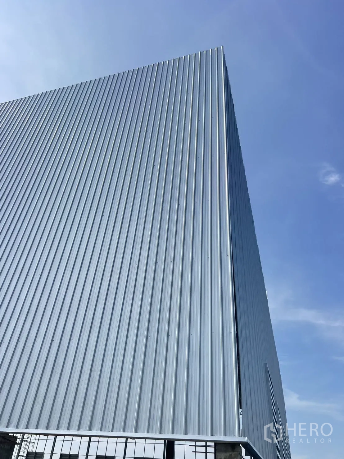 Factory for rent in Mueang Samut Prakan, Samut Prakan - Tall corrugated metal facade of a modern factory against a blue sky.