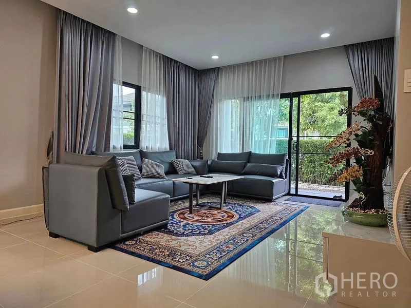 Detached House for rent or sale in Lam Luk Ka, Pathum Thani - Bright living room with large windows, sheer curtains and sliding door to garden