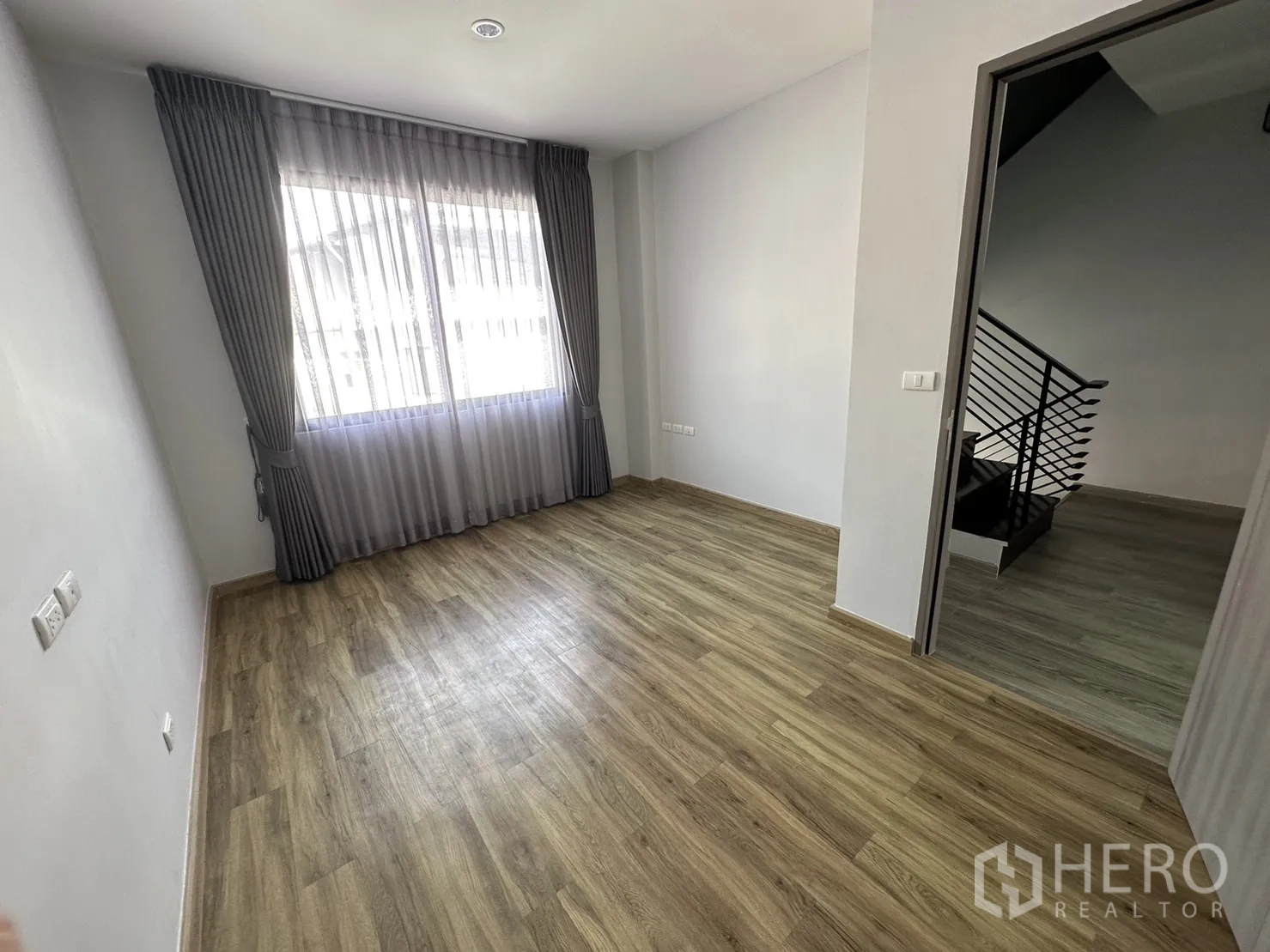 Home Office for rent or sale in Suan Luang, Bangkok - Bedroom with large window, grey curtains and warm wood-style flooring.