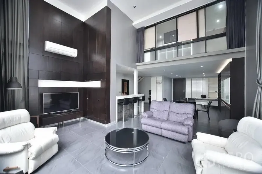Condominium for rent in Khlong Toei, Bangkok - Duplex-style living room with double-height ceiling, dark wood media wall, sofas and mezzanine at The Emporio Place.