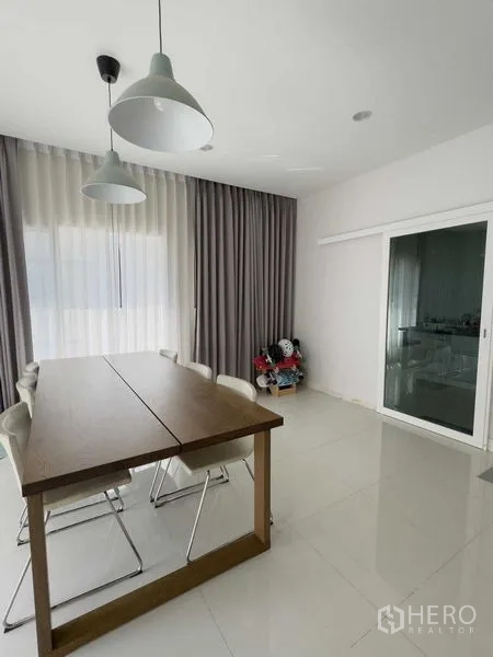 Detached House for rent or sale in Bang Khen, Bangkok - Dining room with wooden table, six chairs, pendant lights and sliding glass door.