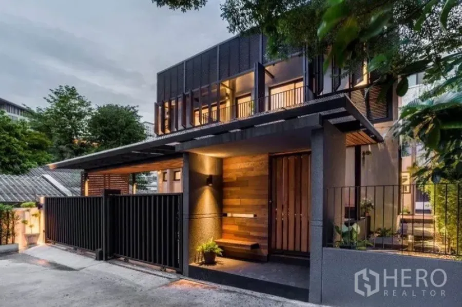ทาวน์เฮาส์ ให้เช่าในKhlong Toei, Bangkok - ด้านหน้าทาวน์เฮาส์สไตล์โมเดิร์นสองชั้นยามเย็น ฟาซาดไม้และโลหะพร้อมรั้วปลอดภัยและไฟสว่าง