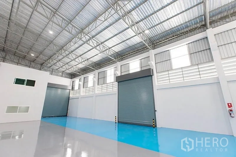 Factory for rent in Bang Phli, Samut Prakan - Multiple loading bays with roller shutters and blue epoxy drive-in zone inside the factory.