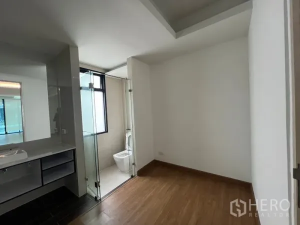 Townhouse for rent or sale in Khlong Toei, Bangkok - Compact bedroom with wood flooring connecting to an ensuite bathroom with glass shower and vanity.