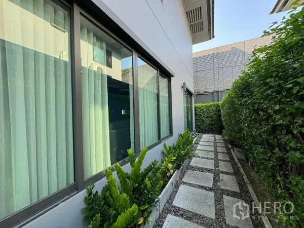 Detached House for rent in Bang Kapi, Bangkok - Walkway along the side yard bordered by hedges and tall windows with curtains.