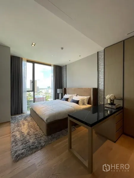 Condominium for rent in Khlong Toei, Bangkok - Bedroom corner with work desk, wardrobes, and floor-to-ceiling window bringing in light and city scenery.
