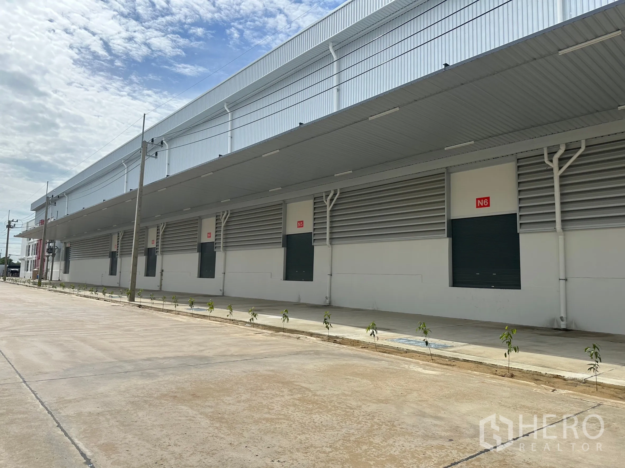 Factory for rent in Khlong Luang, Pathum Thani - Modern warehouse facade with long canopy, multiple loading bays and roller shutters.
