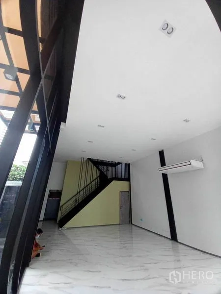 Retail Space for rent in Khlong Toei, Bangkok - Double-height retail showroom with marble-look floors, black steel staircase, wall-mounted AC and glass frontage.