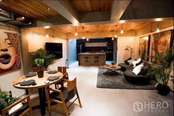 Townhouse for rent in Khlong Toei, Bangkok - Open-plan living and dining room with concrete-and-wood finishes, pendant lights and art, leading to the kitchen.