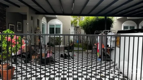 Detached House for rent or sale in Pathum Thani - Covered carport with black metal gate and checkered floor tiles beside a small garden.