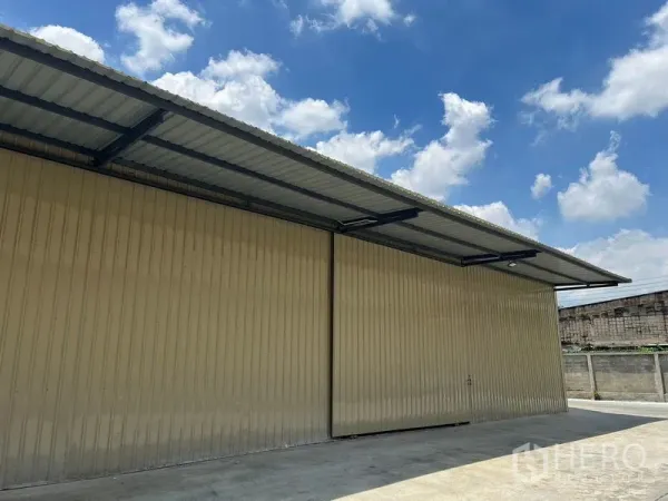 Warehouse for rent in Phra Khanong, Bangkok - Close-up of the warehouse’s corrugated metal facade and canopy roof beside the paved loading area.
