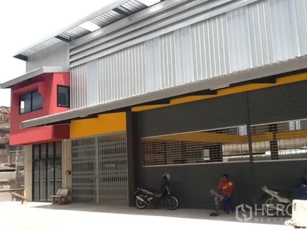 Warehouse for rent in Bang Kapi, Bangkok - Modern warehouse exterior with metal cladding, red office wing, wide roller shutters and a covered loading bay in Bang Kapi.
