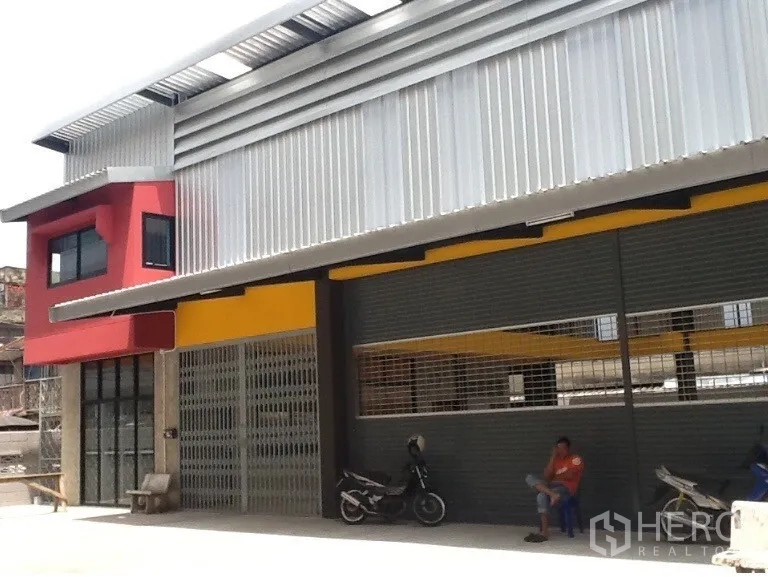 Warehouse for rent in Bang Kapi, Bangkok - Modern warehouse exterior with metal cladding, red office wing, wide roller shutters and a covered loading bay in Bang Kapi.