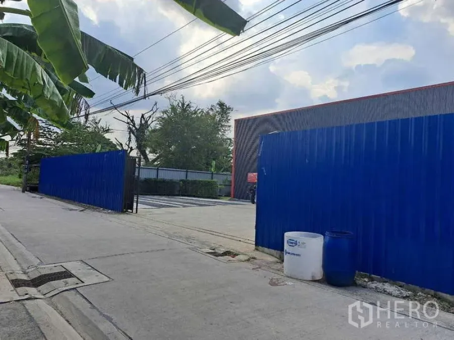 货栈 出售在Khlong Sam Wa, Bangkok - 从街道望向园区入口，可见蓝色滑动围墙大门与车道入口。