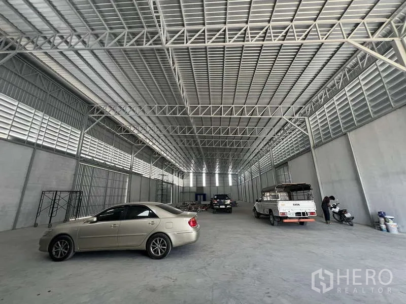 Warehouse for rent in Prawet, Bangkok - Expansive warehouse floor with steel truss roof, vehicles inside, and ample loading space.