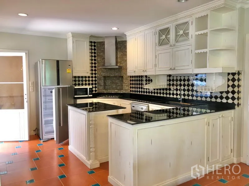 Detached House for rent in Mueang Samut Prakan, Samut Prakan - U‑shaped kitchen with black granite countertops, white cabinetry, black‑and‑white tiled backsplash and stainless appliances.