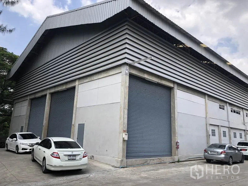 Warehouse for rent in Khlong Sam Wa, Bangkok - Corner view of a modern industrial warehouse in Khlong Sam Wa with high metal-clad roof, multiple roller shutter doors and on-site parking.