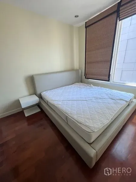 Condominium for rent in Khlong Toei, Bangkok - Secondary bedroom with upholstered bedframe, bedside table, roller blinds and abundant natural light.