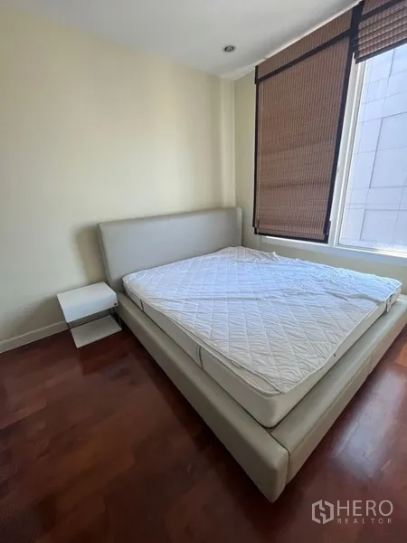 Condominium for rent in Khlong Toei, Bangkok - Secondary bedroom with upholstered bedframe, bedside table, roller blinds and abundant natural light.