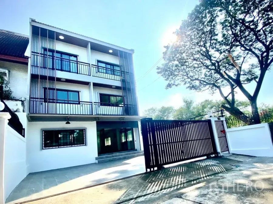 Townhouse for rent in Prawet, Bangkok - Three-storey townhouse facade with gated driveway and balconies in a leafy setting.