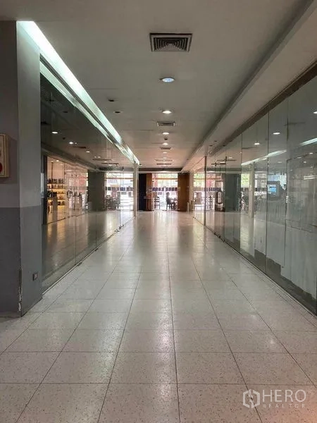 Retail Space for rent - Long mall hallway with glass storefronts on both sides, recessed lighting and air-conditioning vents leading to the entrance.
