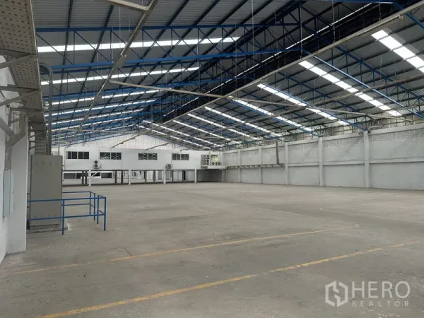 Factory for rent in Nonthaburi - Spacious factory hall with steel truss roof, skylights and a raised office block.
