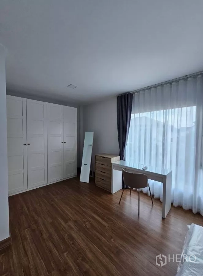 Detached House for rent in Bang Phli, Samut Prakan - Master bedroom wall of white wardrobes and a study desk by the window.