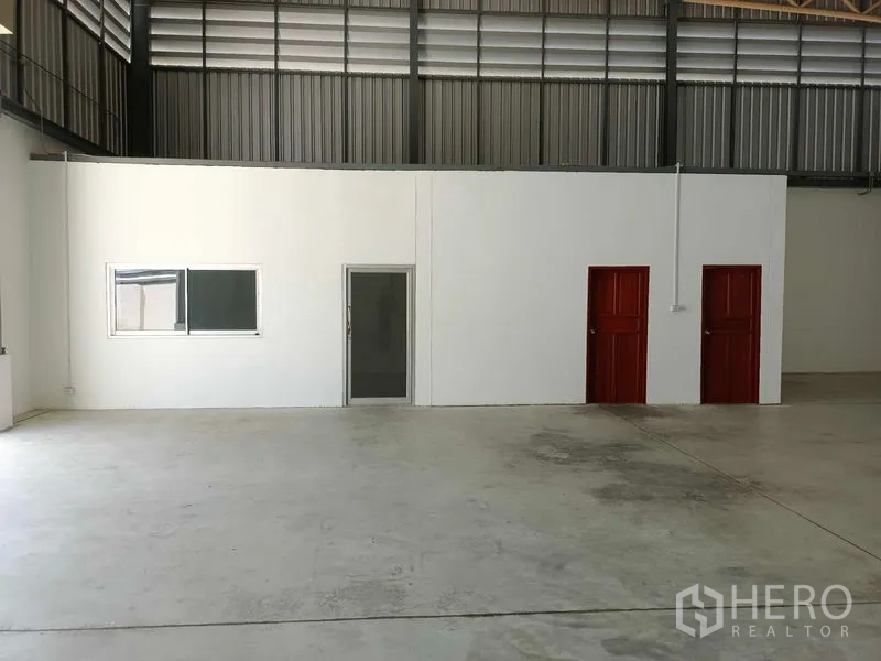 Warehouse for rent in Suan Luang, Bangkok - Internal office block with glass door, window, and two red restroom doors inside the warehouse.