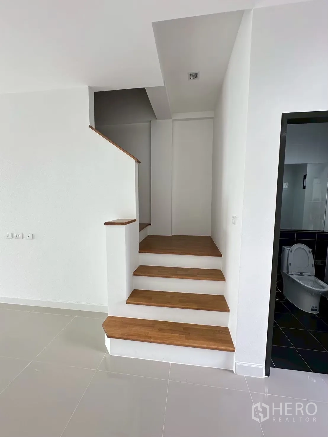 Home Office for rent in Lat Phrao, Bangkok - Entrance area with glossy tiles leading to wooden steps beside a bathroom door.
