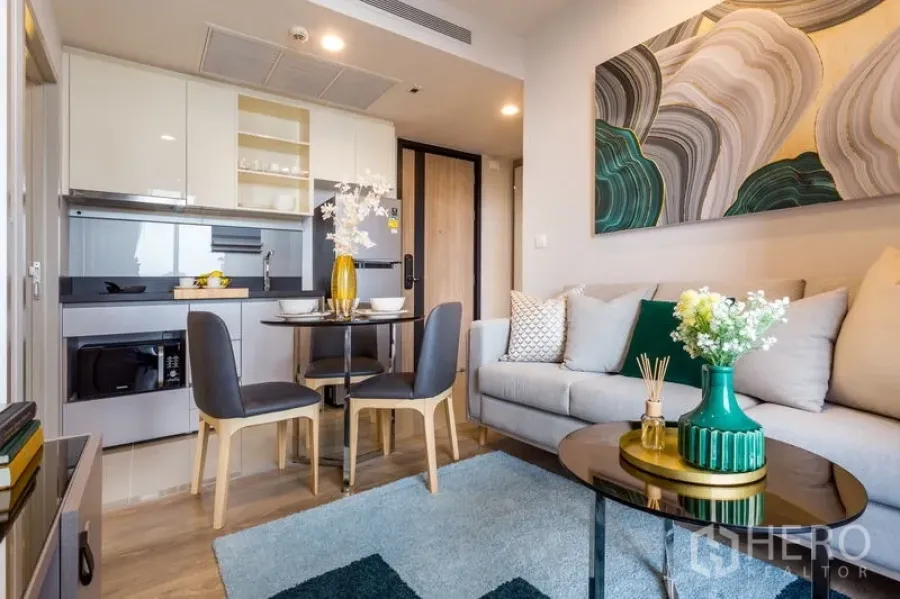 Condominium for rent in Khlong Toei, Bangkok - Modern open-plan living area with built-in kitchen, round dining table, and sofa with abstract art.