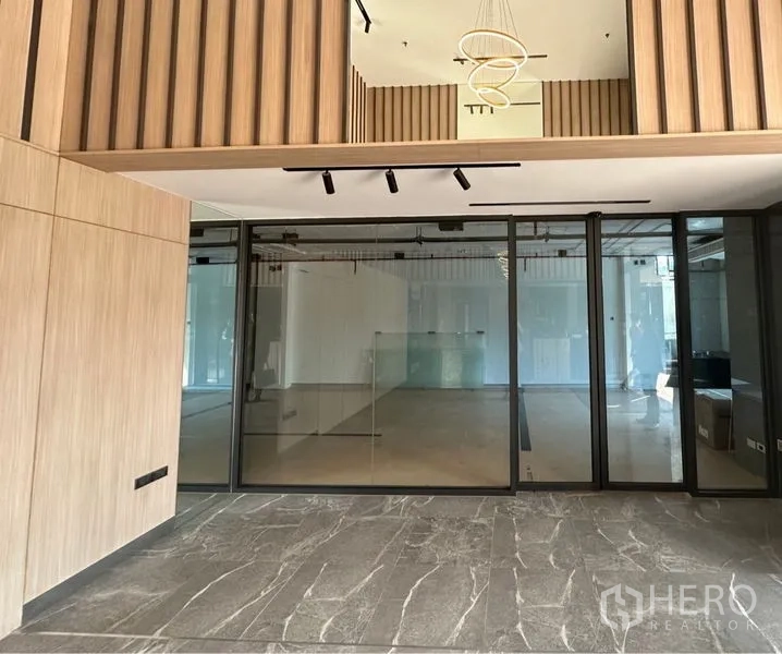 Office Space for rent in Khlong Toei, Bangkok - Double-height office entrance with wood slat accents, a modern chandelier and full-height glass partitioned rooms.