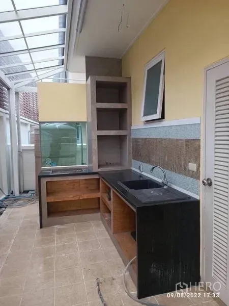 Detached House for sale in Prawet, Bangkok - Semi-outdoor Thai kitchen with black countertop, sink, open shelves and a skylight roof.
