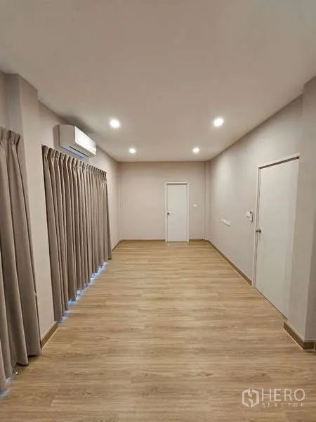Detached House for rent in Bang Phli, Samut Prakan - Large unfurnished room with wood flooring, air conditioner and long curtains.