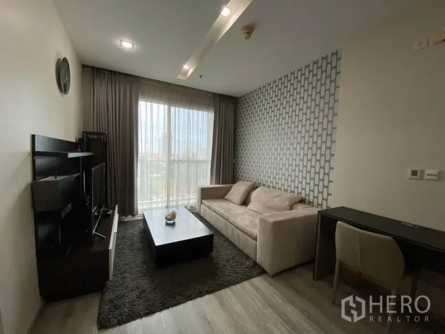 Condominium for rent or sale in Khlong Toei, Bangkok - Bright living room with sofa, TV unit, work desk and balcony window with city view.