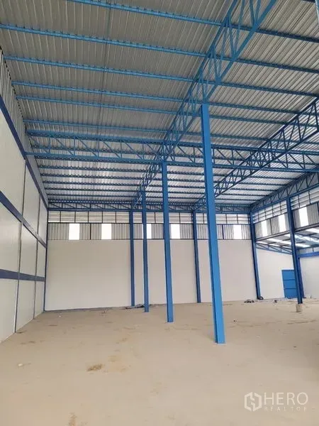 Factory for rent or sale in Khlong Luang, Pathum Thani - High-clearance warehouse interior featuring blue steel trusses and concrete floor.