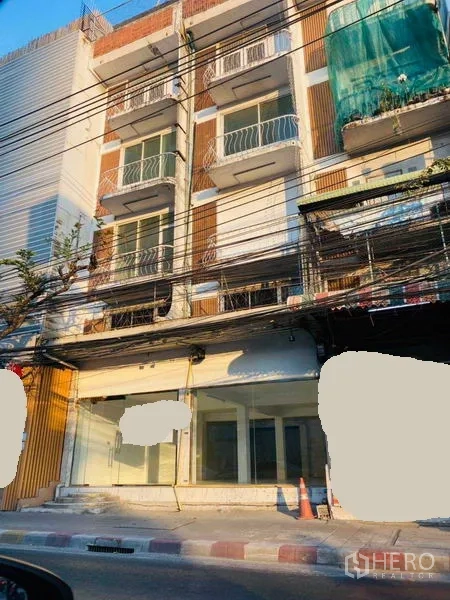 Shophouse for rent in Khlong Toei, Bangkok - Streetfront four-storey shophouse facade with glass storefront and small balconies.