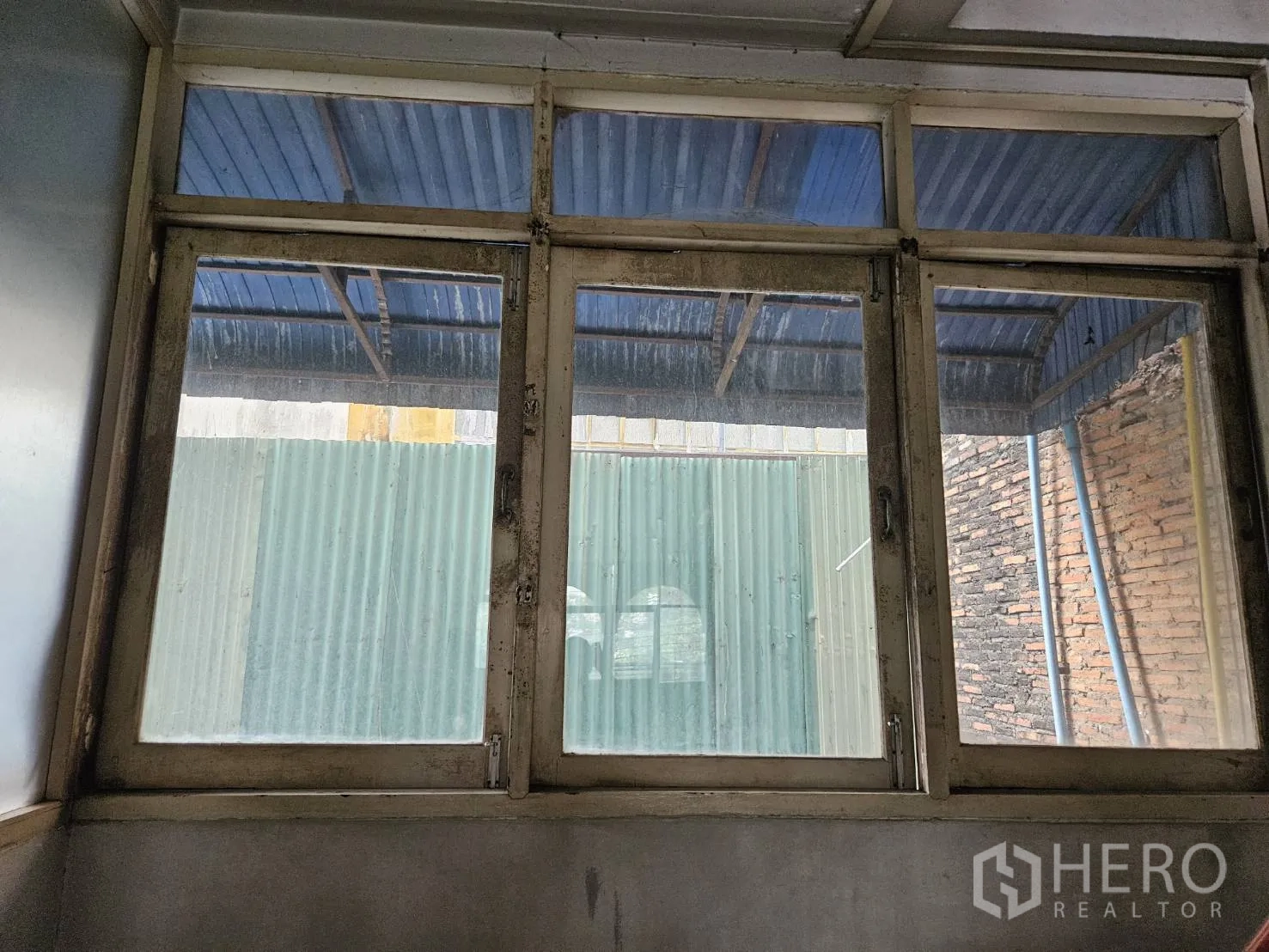 Shophouse for rent in Watthana, Bangkok - Close-up of interior window facing a corrugated awning and brick wall at the rear.